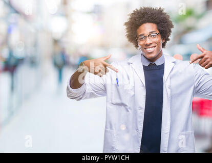 Afro American medico scienziato uomo sullo sfondo isolato guardando fiduciosi con il sorriso sul volto, rivolto a se stessi con le dita orgogliosa e felice. Foto Stock