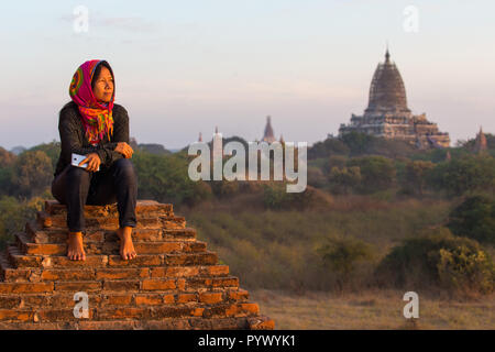 Donna seduta sul tempio di mattoni meditando al tramonto su Bagan pianura in Myanmar Foto Stock