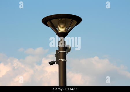 Moderno in metallo di colore nero via lampada post con LED fulmini e la piccola telecamera di sorveglianza con rivelatore di movimento montati su un lato su nuvoloso cielo blu Foto Stock