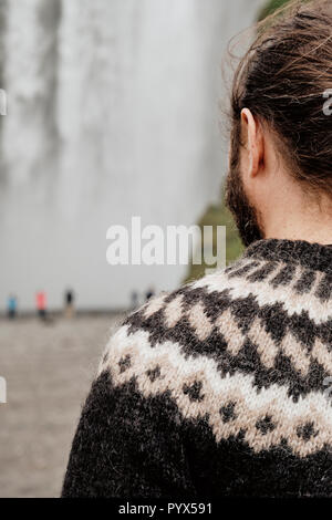 Un islandese guida turistica indossando un tradizionale Lopapeysa islandese maglione di lana a cascata Skogafoss nel sud dell'Islanda. Versione di messa a fuoco Foto Stock