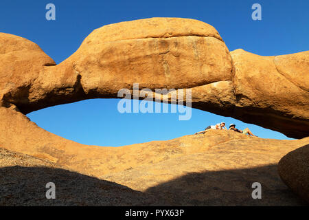 Namibia Paesaggi; due turisti che pongono alla roccia arch a Spitzkoppe, Namibia Africa Foto Stock