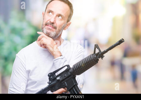 La mezza età senior annoso uomo delinquente tenendo la pistola arma isolato su sfondo faccia seriamente pensando di domanda, molto confusa idea Foto Stock