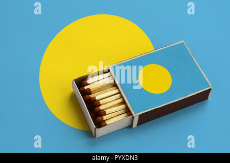 Palau flag è mostrato in un aperto la scatola di fiammiferi, il quale è riempito con corrispondenze e giace su di una bandiera di grandi dimensioni. Foto Stock