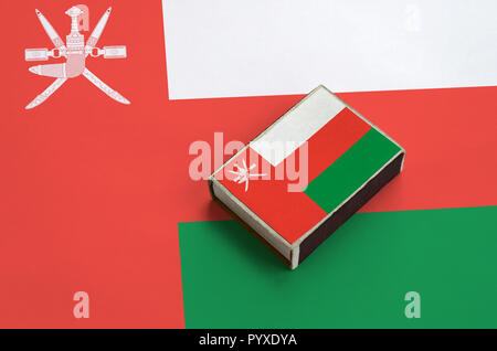 Oman flag è raffigurato su una scatola di fiammiferi che giace su di una bandiera di grandi dimensioni. Foto Stock