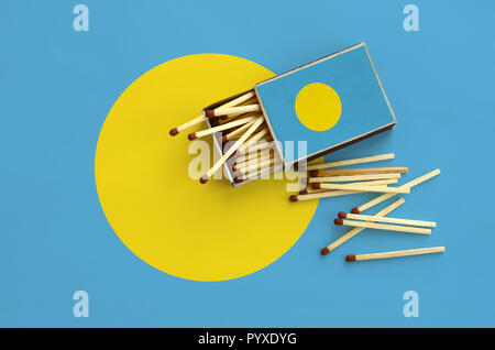 Palau flag è mostrato su un open matchbox, da cui diversi corrisponde a caduta e giace su di una bandiera di grandi dimensioni. Foto Stock