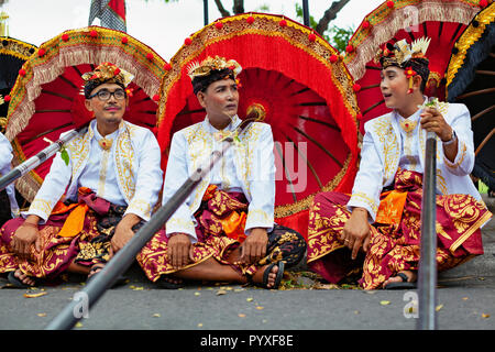 Bali, Indonesia - 23 Giugno 2018: un gruppo di giovani uomini ballerino in costumi etnici con tradizionale rosso nero e giallo ombrelloni sulla cerimonia Indù parade Foto Stock