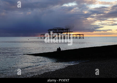 West Pier di Brighton al tramonto, con una romantica coppia che si staglia contro le rovine e una murazione di uccelli Foto Stock
