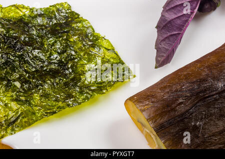 Still Life - aguglia affumicato con calce, basilico, cipollotti, peperoncino, nori chips, spezie, olio d'oliva in un bianco piatto di ceramica, su di un tavolo di legno Foto Stock