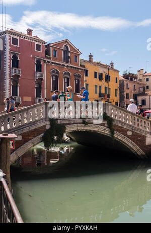 I turisti la linea a ponte su uno dei molti canali di Venezia, gode di una posizione soleggiata giornata estiva in Italia Foto Stock