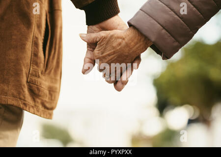 Close up di senior l uomo e la donna per mano e camminare all'esterno. Vista posteriore della vecchia coppia camminando mano nella mano all'esterno. Foto Stock