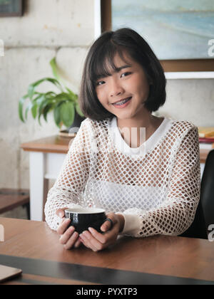 Felice adolescente asiatica ragazza con una bevanda calda in mano e sorridente, il concetto di stile di vita. Foto Stock