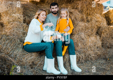 Bella donna versando il latte in vetro mentre suo marito e la figlia seduta vicino a livello di azienda Foto Stock