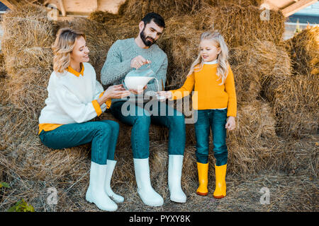 Maschio adulto agricoltore versando il latte alla piccola figlia mentre sua moglie seduta vicino al ranch Foto Stock