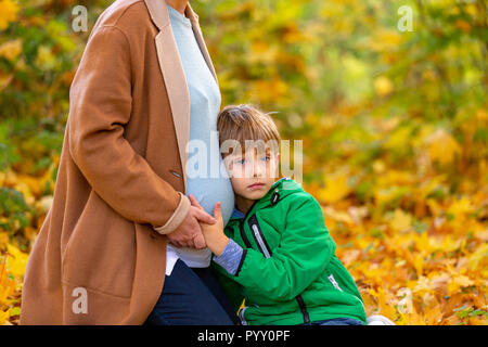 Carino dolce bambino caucasico ascoltando la sua gravidanza della madre aspetta belly baby agitando nel pancino. Le aspettative, in attesa di un bambino, in attesa di un Foto Stock