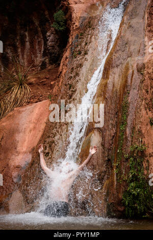 Escursionista che intraprende una pausa rinfrescante in una piccola cascata di un canyon laterale del Grand Canyon, il Parco Nazionale del Grand Canyon Foto Stock