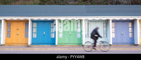 Bournemouth Regno Unito. Persone in bicicletta nella parte anteriore della pittoresca spiaggia di capanne situato sulla passeggiata sul mare di Bournemouth anteriore. I ciclisti sono fuori fuoco. Foto Stock