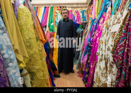 Un vestito, commerciante tessile posa per un ritratto nel suo negozio nel Souk a Doha, Qatar. Foto Stock