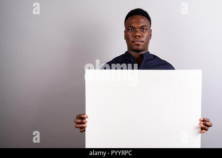 Giovane imprenditore africano tenendo la scheda bianco contro il retro bianco Foto Stock