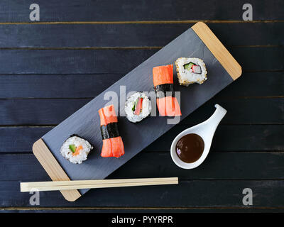 Scheda di presentazione di sushi con riso e salmone e panini con tonno e salsa piccante al buio su un sfondo di legno,. Il cibo giapponese di stile. Vista superiore Foto Stock