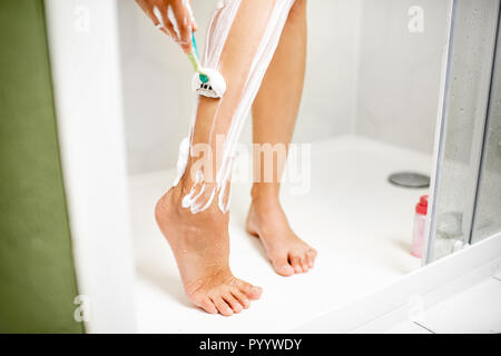 La donna la rasatura le gambe con il rasoio e schiuma nella cabina doccia Foto Stock