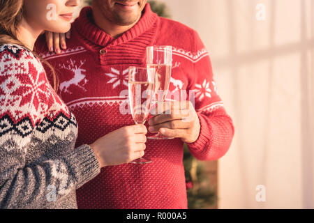 Vista ritagliata della giovane nel natale maglioni holding occhiali con champagne Foto Stock