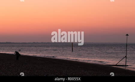 L'uomo con il rivelatore di metalli enthusiast portano il suo rivelatore di metalli su una spiaggia di ciottoli di sunrise Foto Stock
