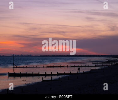 Un giovane da solo su una spiaggia di sabbia a godersi il tramonto Foto Stock