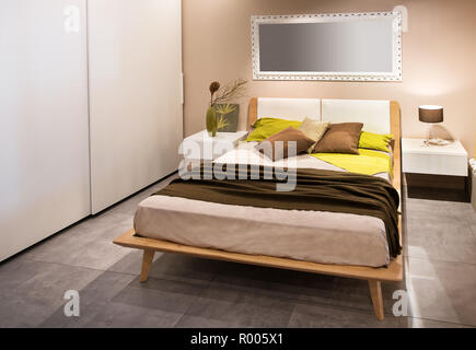 Camere da letto moderne con pavimenti in legno di stile Scandinavo e letto Armadi laterali in beige e grigio con decor di colore giallo cuscini di accento sul divano Foto Stock