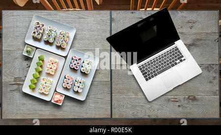 Consegna qualche piatto di sushis e portatile su due tavoli in legno Foto Stock