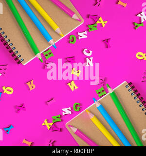 Due notebook e multicolori matite in legno su un sfondo rosa, le lettere dell'alfabeto inglese sono sparse Foto Stock