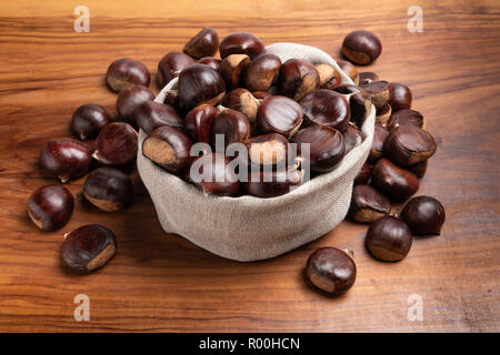 Cumulo di castagne fresche in un piccolo sacco biancheria su una tavola in legno rustico Foto Stock