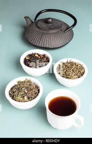 Ghisa teiera con tazza da tè e tre tazze di tè nero, bancha tè verde ed imperatore del tè bianco su un verde chiaro Tavolo in legno Foto Stock