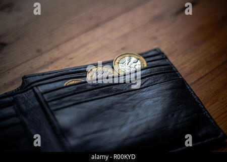 Nuovo grande sterlina GBP monete posa casualmente sulla sommità del portafoglio nero sulla superficie di legno. Ricchezza, denaro contante, modificare. Foto Stock