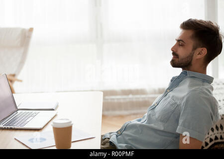 Giovane uomo positivo di relax presso la scrivania in ufficio Foto Stock