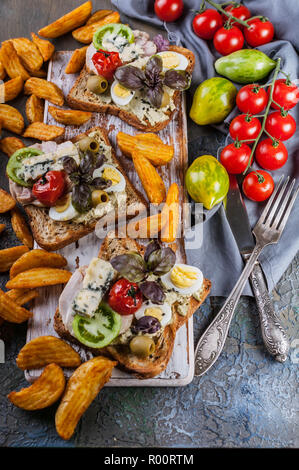 Stuzzicanti toast con avocado, uova di quaglia, pomodori, Dor formaggio blu e patatine fritte. Autore della cucina. Originale serve piatti Foto Stock