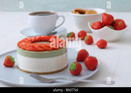 Demo di cottura. No-bake a due strati mini Strawberry Cheesecake matcha. Fette di fragola decorano la parte superiore della torta. 3 tazze di caffè, biscotti e s Foto Stock