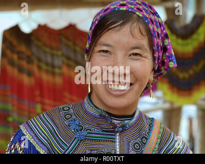 Giovane vietnamita Flower H'mongs hill-tribe donna indossa fiore ricamato H'mongs costumi in blu e sorrisi per la fotocamera. Foto Stock