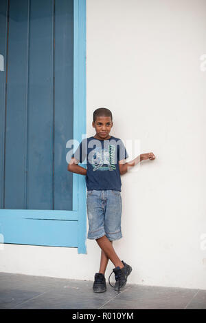 Un bambino cubano si erge contro un muro come si guarda gli altri bambini a giocare. Foto Stock