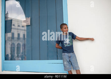 Un bambino cubano si erge contro un muro come si guarda gli altri bambini a giocare. Foto Stock