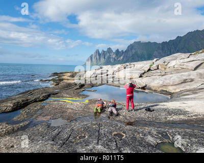 Costa a Tungeneset,vista sulla formazione rocciosa a mountain range Okshornan, i turisti a scattare foto di riflessioni, isola Senja, Troms, Norw settentrionale Foto Stock