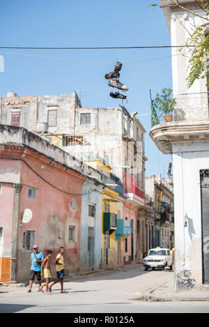 Tre giovani amici a piedi attraverso il centro di l'Avana. Un paio di scarpe da ginnastica pende su un filo di byte di overhead. Foto Stock