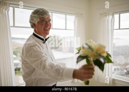 Sorridente uomo maturo tenendo un mazzo di fiori all'interno di una camera in casa sua. Foto Stock