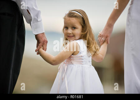 Ritratto di una giovane ragazza tenendo le mani con la sposa e lo sposo mentre vestito come un fiore ragazza. Foto Stock