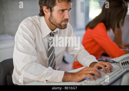 Giovane uomo d affari digitando mentre i suoi colleghi lavorare accanto a lui in un ufficio. Foto Stock