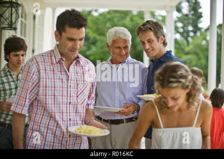 Senior adulto uomo in piedi con la sua metà-figlio adulto in attesa di ottenere un po' di pasta mentre la sua famiglia piatto fino a cena. Foto Stock