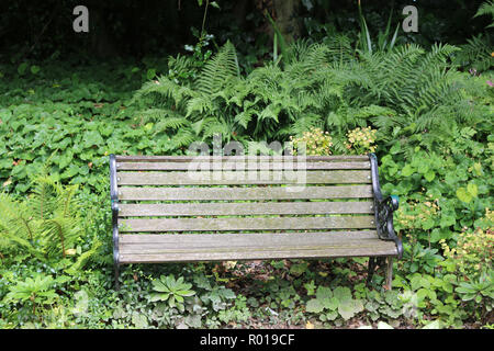 In legno tradizionale sede del parco su di un telaio metallico in un angolo ombreggiato circondato da piante. Foto Stock