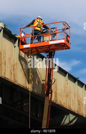 Manutenzione dell'infrastruttura lavoratore con cablaggio di sicurezza lavorando su una città elevata del sistema ferroviario in un sollevamento del braccio o cherry picker. Foto Stock