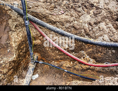 Costruzione di linee metalliche e cavi a fibre ottiche di collegamento per reti di comunicazione. La trincea trasporta i condotti per il gas acqua sewa elettrico Foto Stock