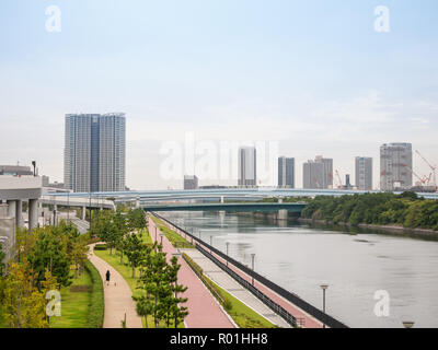 Una donna a piedi il suo cane in un bellissimo parco vicino a un canale. Un treno attraversare un ponte. Tokyo, Giappone Foto Stock