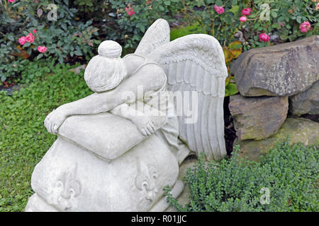 Un giardino statua di pietra di un Angelo seduto appoggiato su di una roccia. Essa può essere vista come il pianto, dorme, o esaurito. Foto Stock